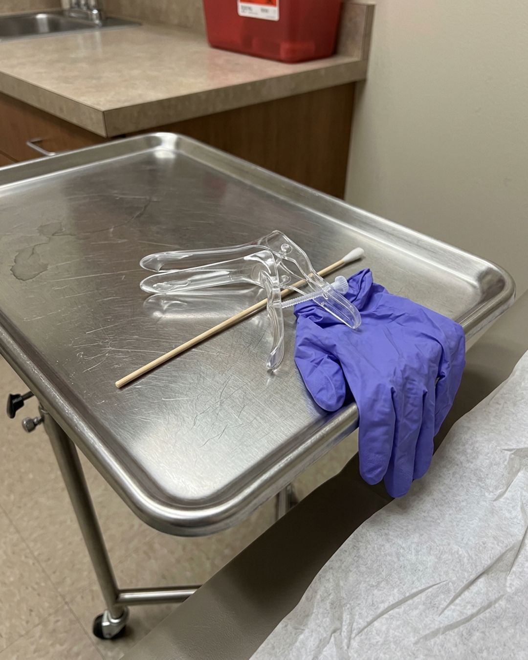 A metal exam tray with a used plastic speculum, a swab and a blue glove