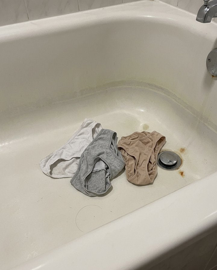 Three pairs of women's underwear tossed in an empty bathtub near the drain