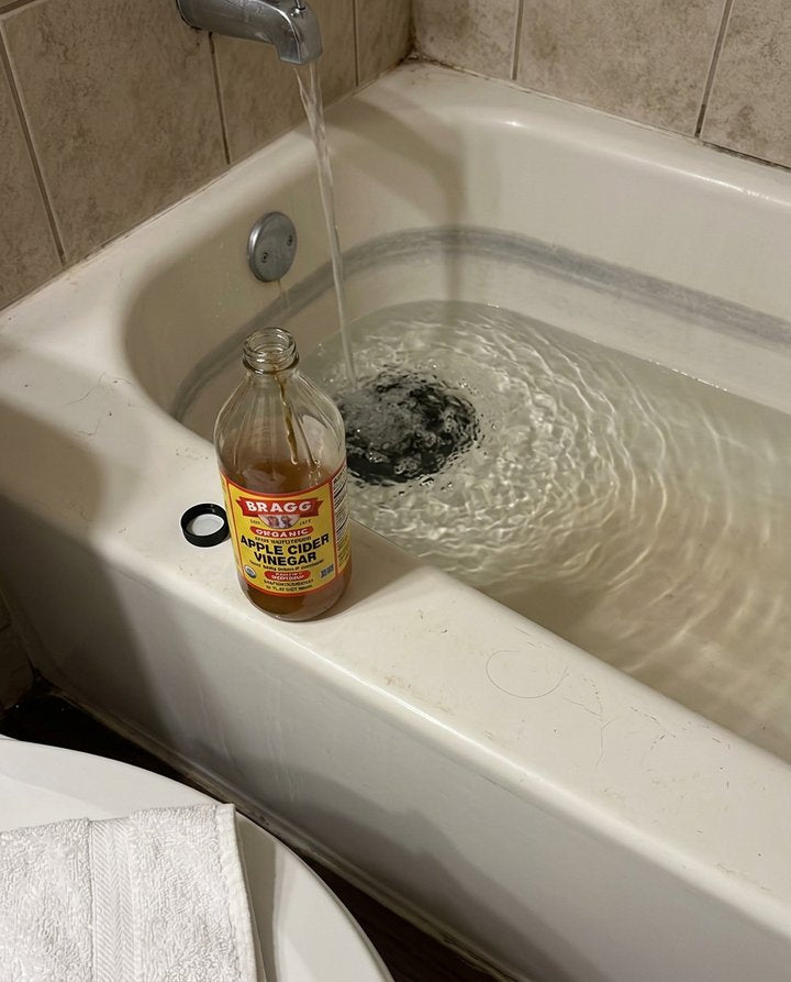 A bottle of Bragg apple cider vinegar on the edge of a bathtub as it fills