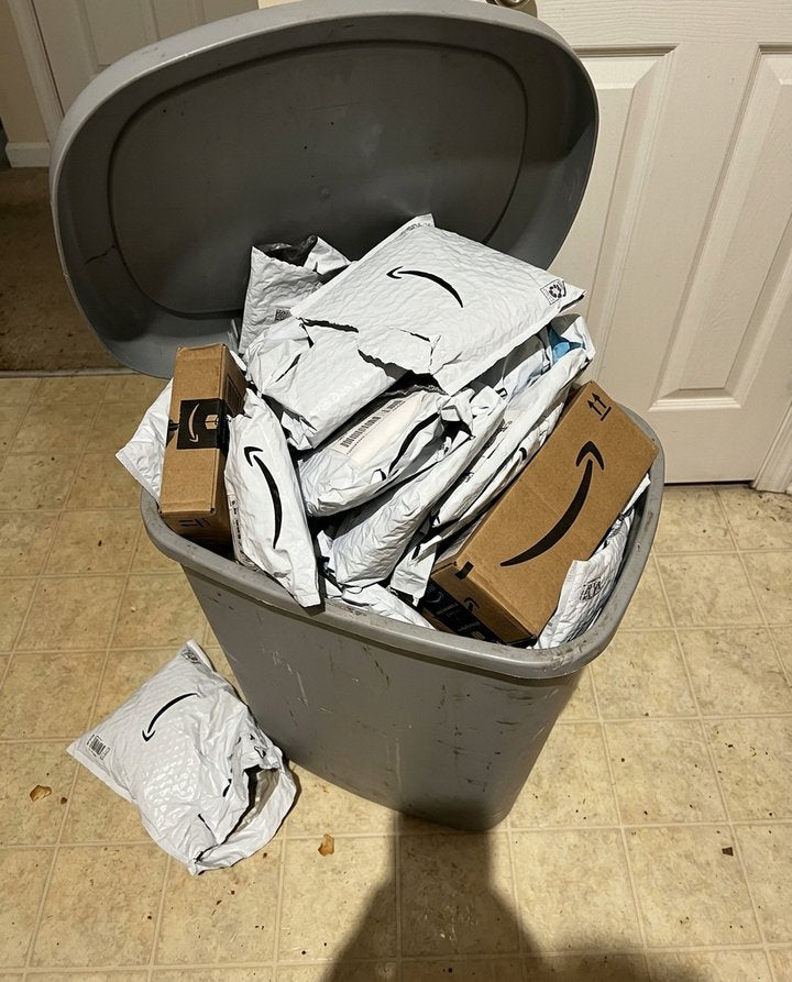 A kitchen trash can overflowing with torn Amazon mailers and boxes