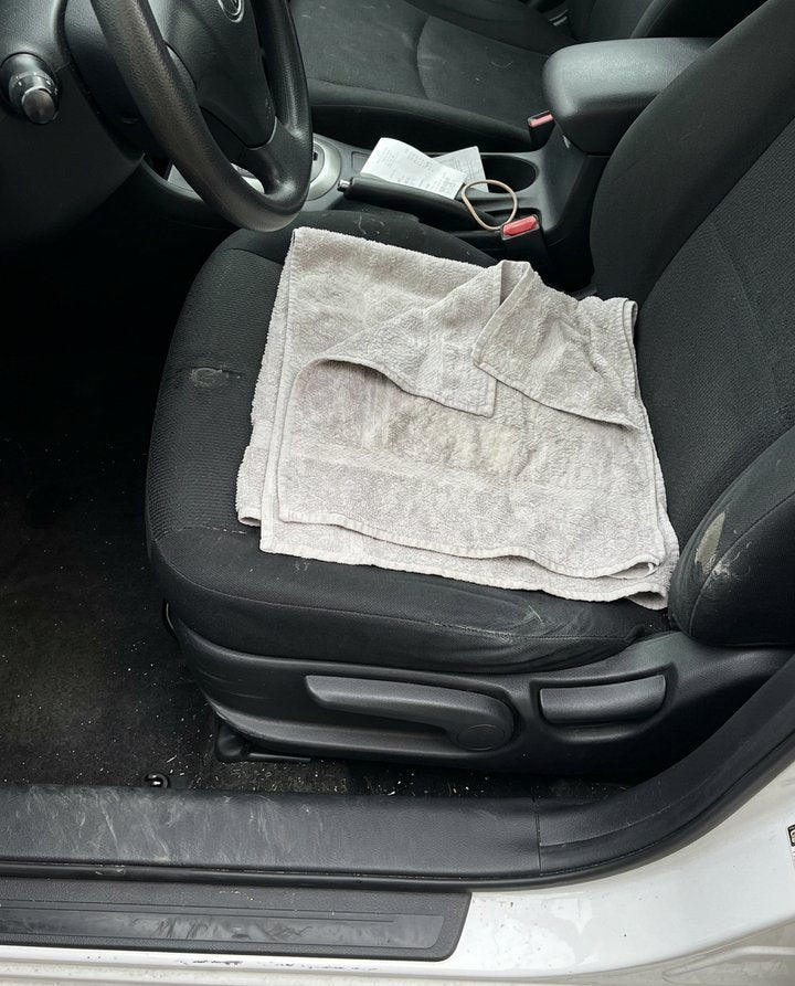 A folded bath towel on the driver's seat of a car, the door open