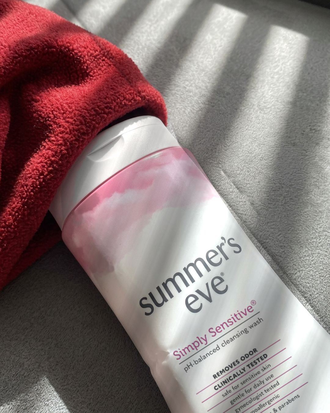 A bottle of Summer's Eve Simply Sensitive wash lying on a couch next to a red throw